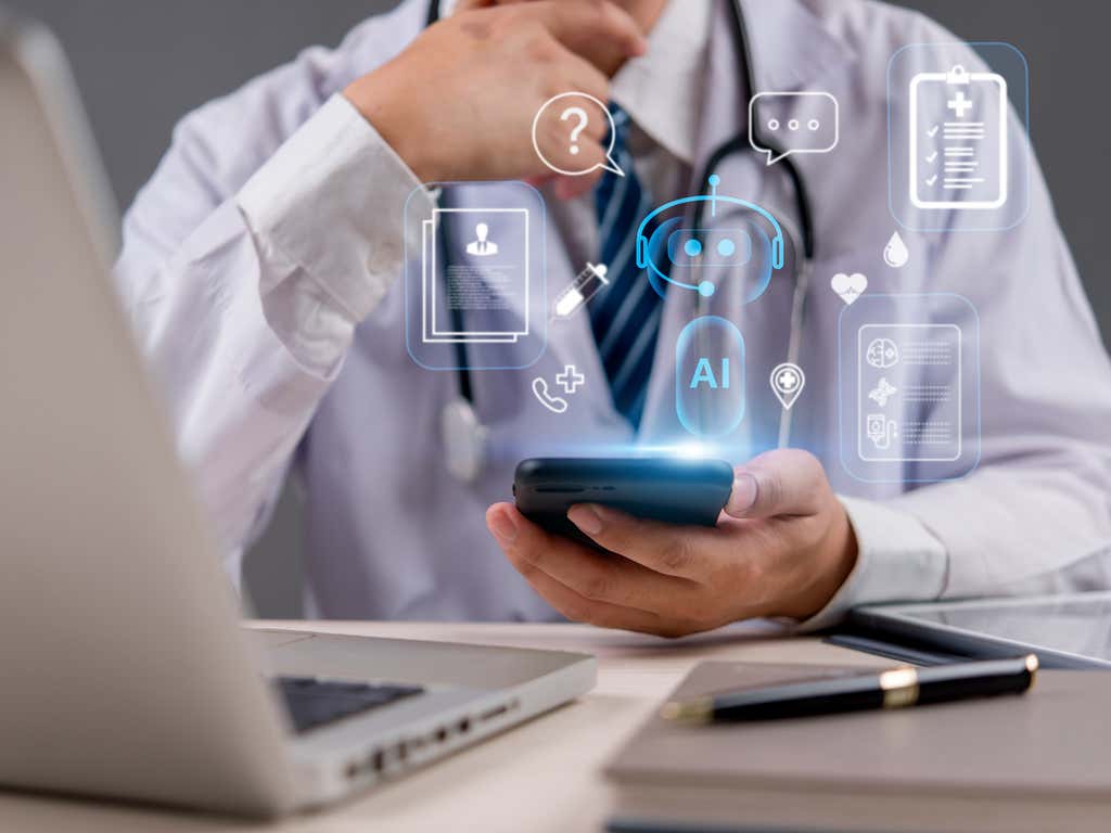 Doctor sitting at their desk holding a phone. The phone has AI icons surrounding it. 