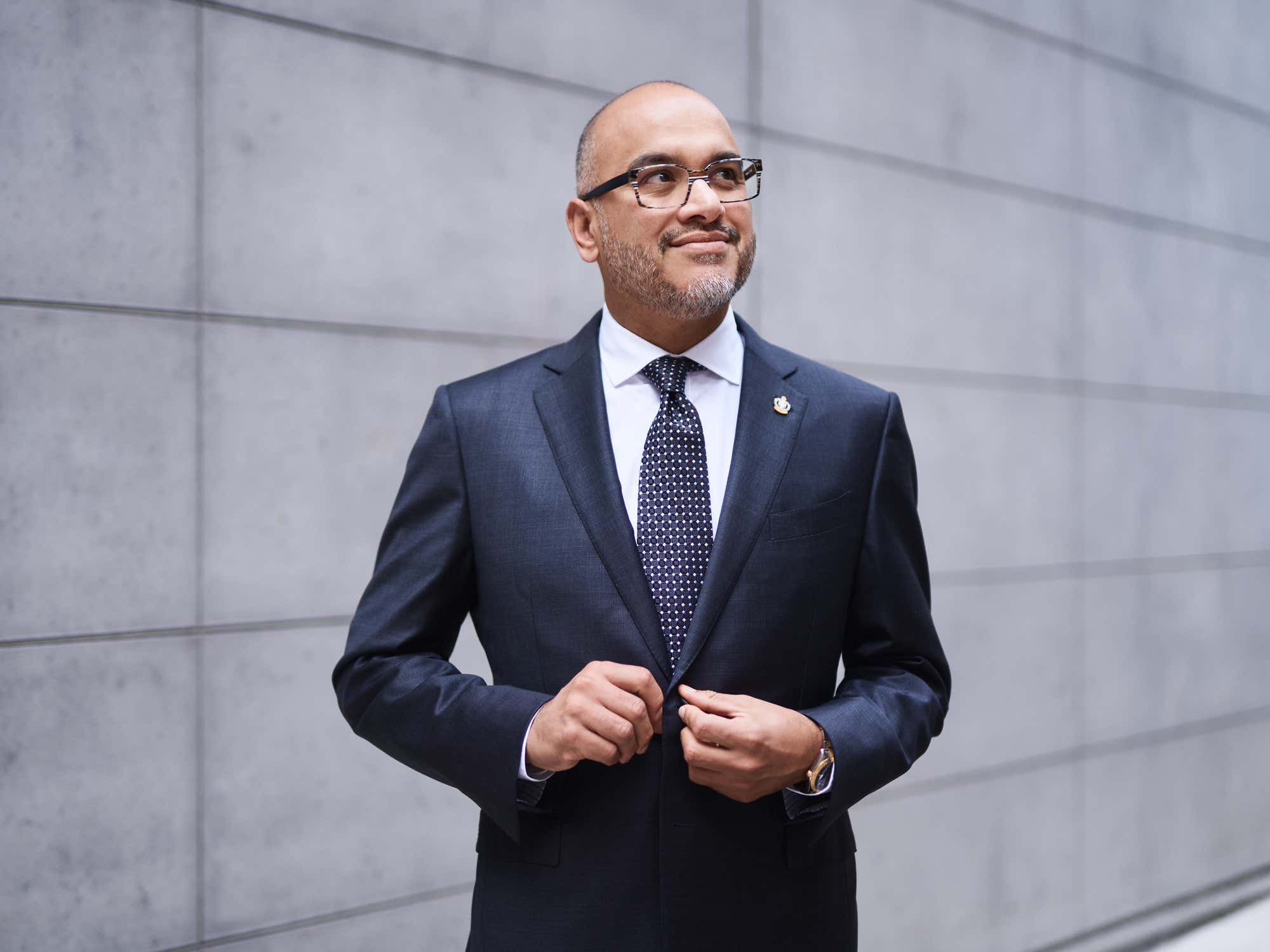 Dr. Ian Preyra smiling standing outside in front of a grey slate wall.