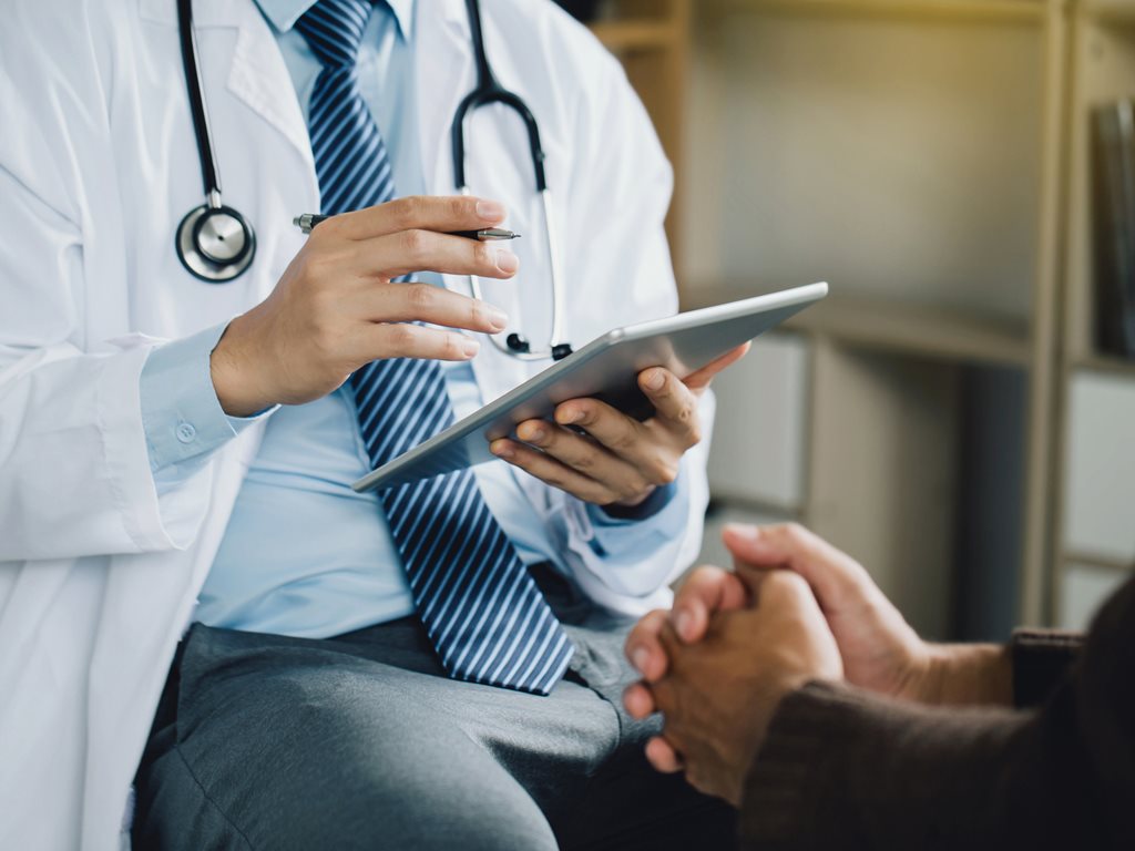 Physician taking notes on a tablet while speaking to patient.