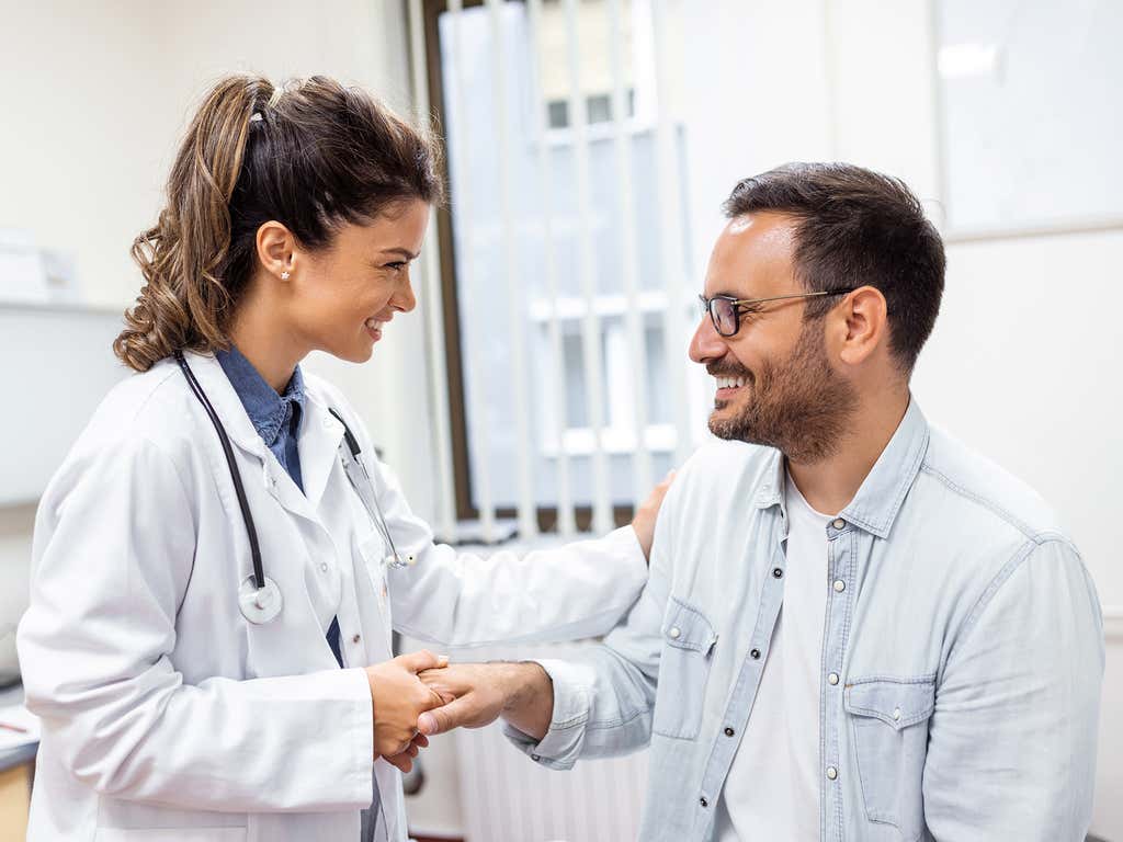 Female physician shaking hands, smiling, with male patient in the doctors office.