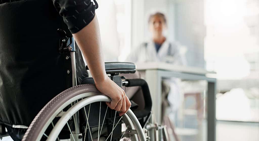 person in a wheel chair talking to a doctor at their desk.