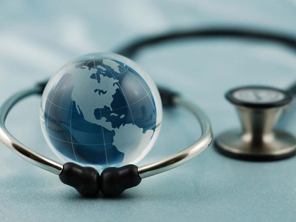 Close-up of a glass globe resting inside a stethoscope on a light blue surface.