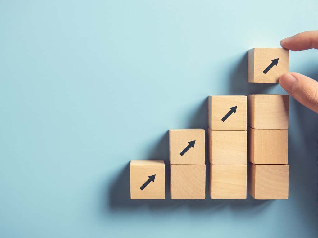 Hand arranging wood block stacking as step stairs with arrows points upwards. Business concept for growth success process.