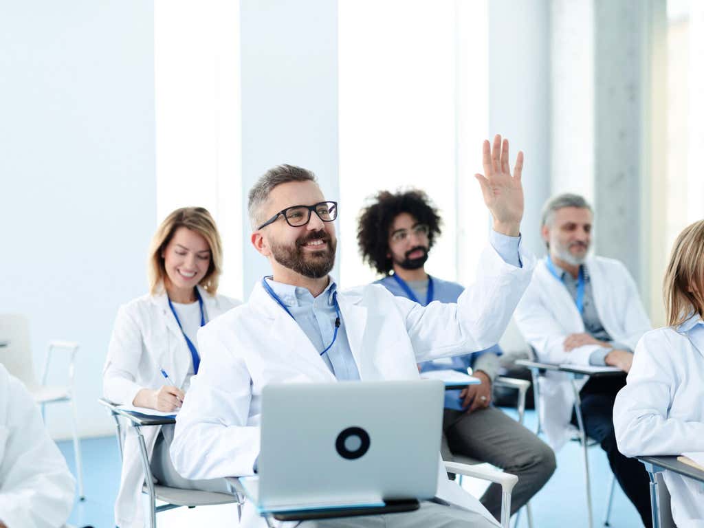 Medical team in conference, doctor asking question to speaker.