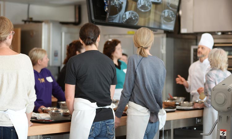 Cooking class listens to chef instructor in kitchen.