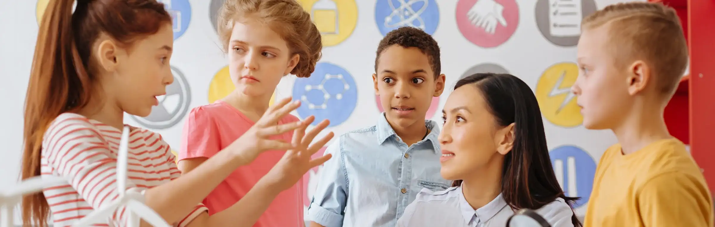 Photo of a student interacting with their teacher and a group of students.